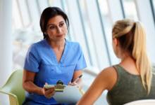 Patient with blonde h空气 meeting with female medical practitioner wearing blue scrubs